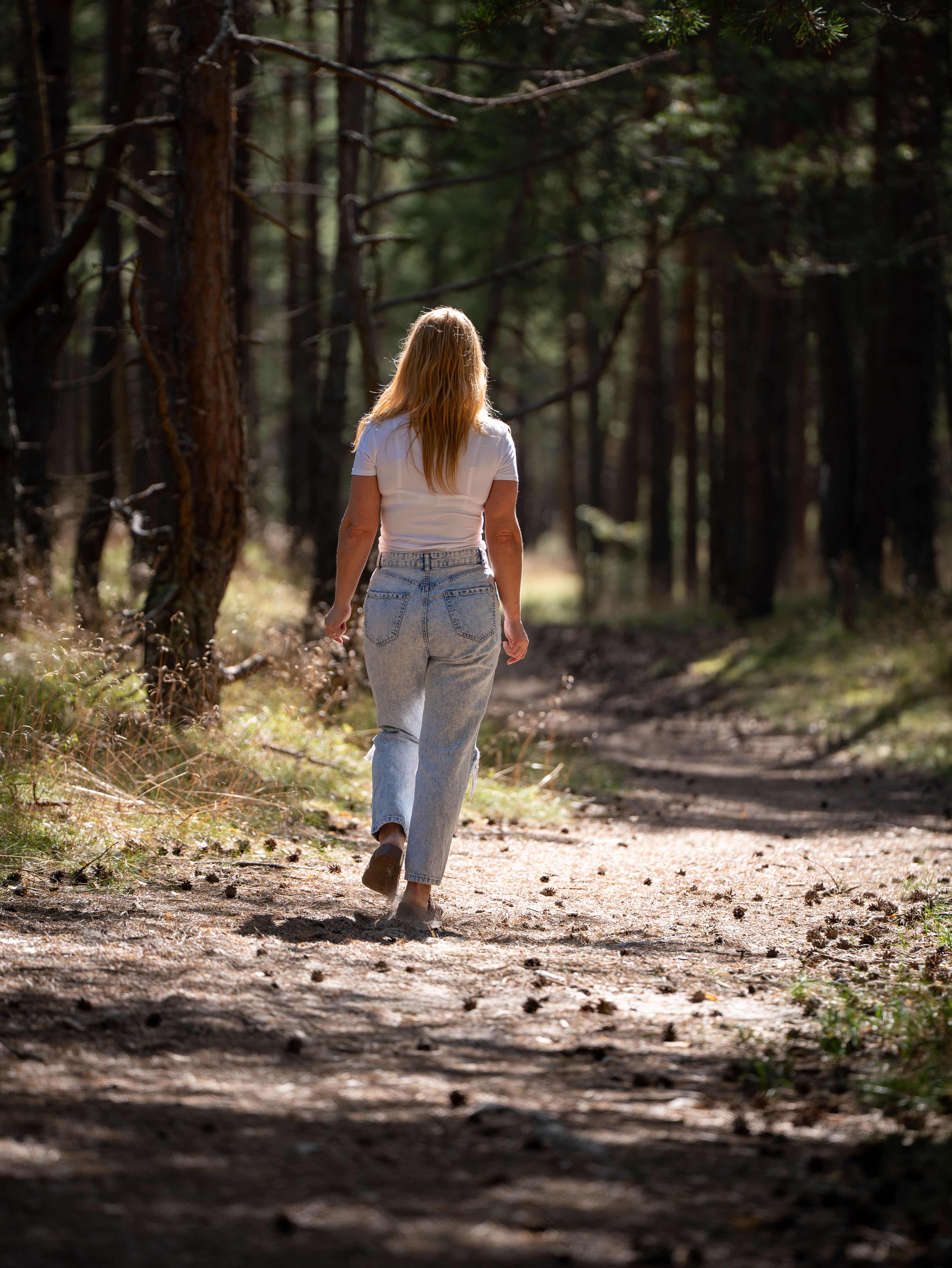 A woman walking alone along a sunlit forest trail